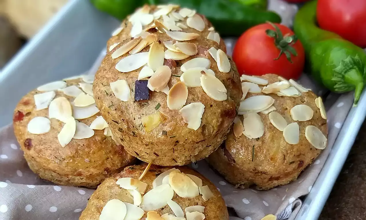 Zlatohnedé slaninové muffiny posypané tenkými plátkami mandlí, usporiadané na bodkovanej látke v plechu, obklopené čerstvou zeleninou