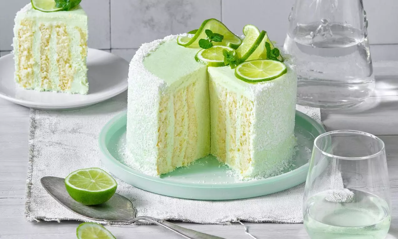 Svetlozelená točená torta s vyšľahaným krémom, zdobená plátkami limetky a lístkami mäty, uložená na bledozelenom tanieri