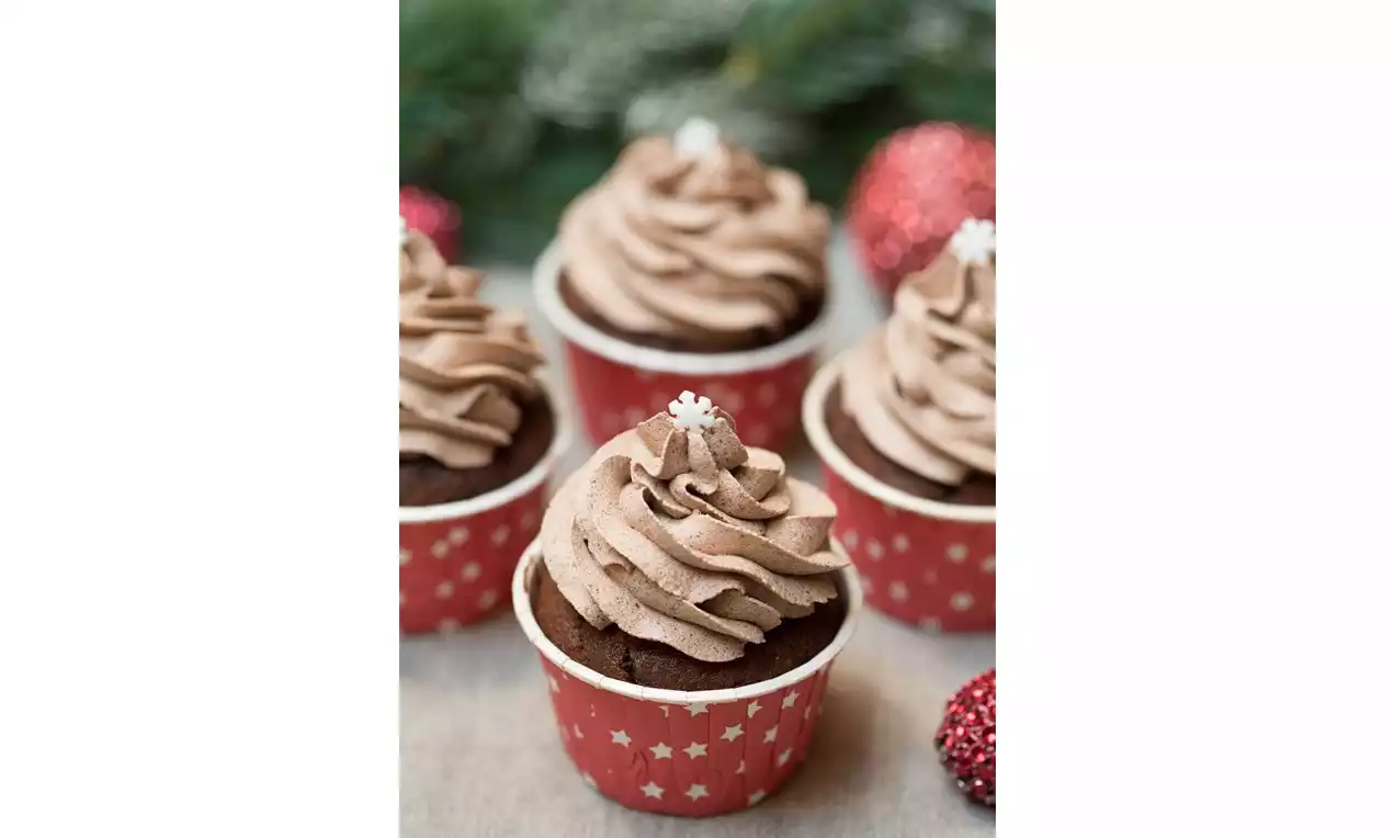 Čokoládové cupcakes vo vzorovaných červených košíčkoch, ozdobené nadýchaným hnedým krémom a bielou cukrovou vločkou na vrchu