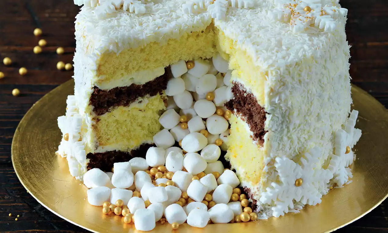 Piňata torta s bavlneným bielym povrchom, žltými a hnedými vrstvami, naplnená zlatými perličkami a mini marshmallows na zlatom podnose