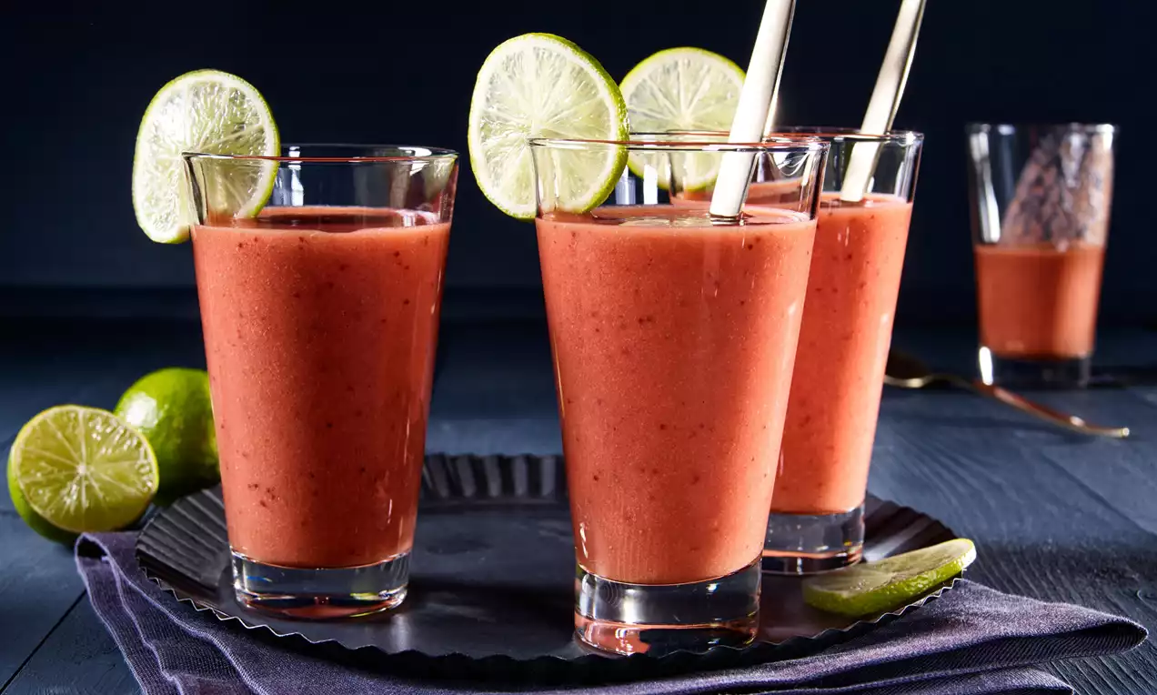 Hladké ovocné smoothie v sýtej oranžovej farbe podávané v sklených pohároch, ozdobené plátkami limetky a umiestnené na tmavom podnose