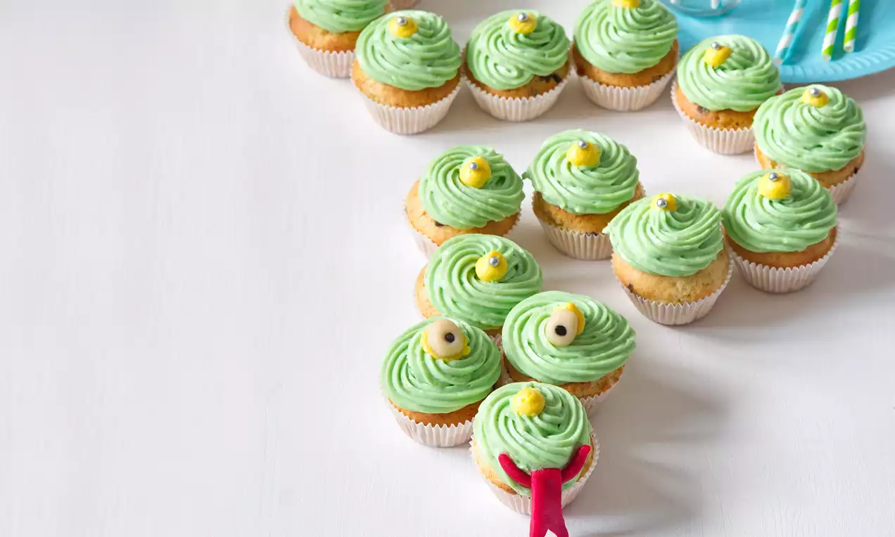 Cupcaky s jemným zeleným krémom usporiadané do tvaru hada, ozdobené očami z cukroviniek a červeným jazýčkom na svetlom stole