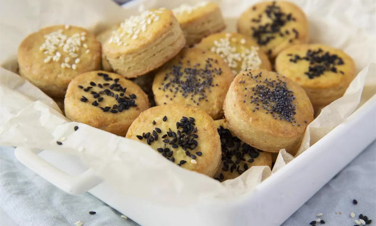 Vegan škvarkové pagáčiky zlatohnedé, guľaté, vrstvené, posypané čiernym a bielym sezamom, úhľadne uložené v bielej keramickej mise na papieri