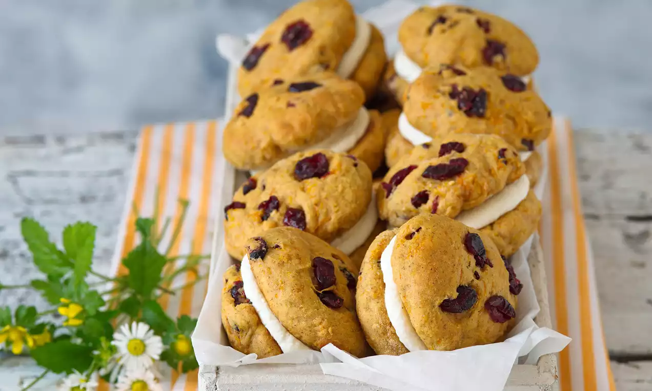 Mrkvové cookies jemne oranžové, okrúhly tvar, mäkko štruktúrované s brusnicami, vrstvené bielym krémom v drevenej debničke s kvetmi
