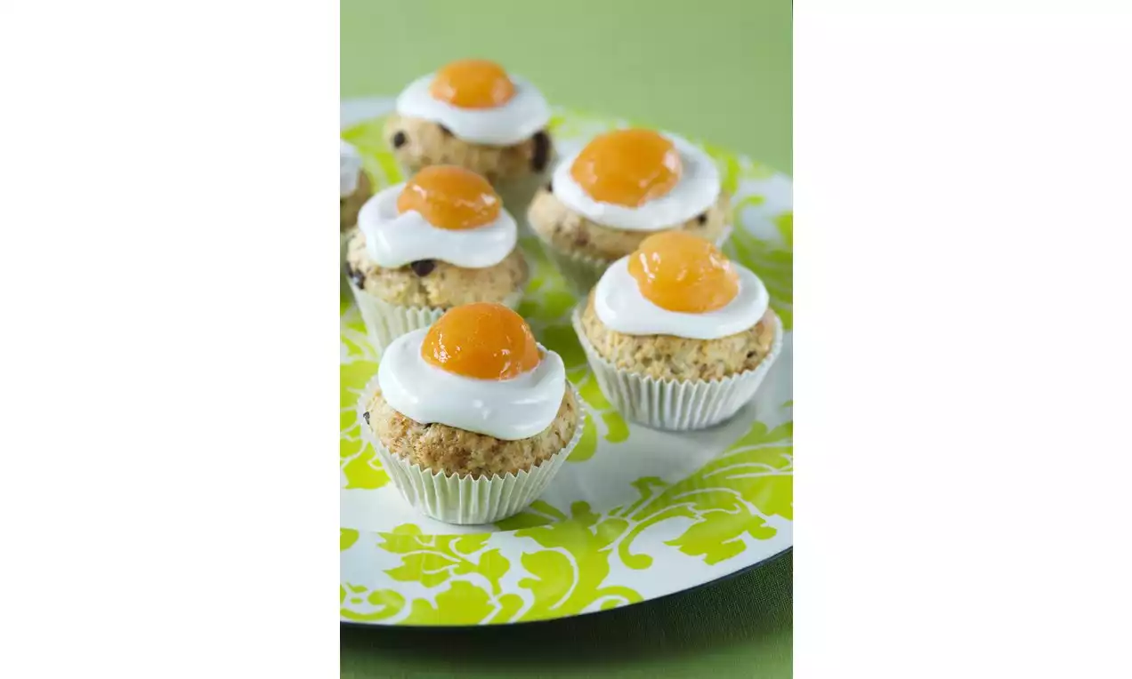Muffiny s jemnou zlatistou kôrkou, ozdobené bielou vrstvou krému a výraznými oranžovými polovicami marhúľ na vzorovanom tanieri