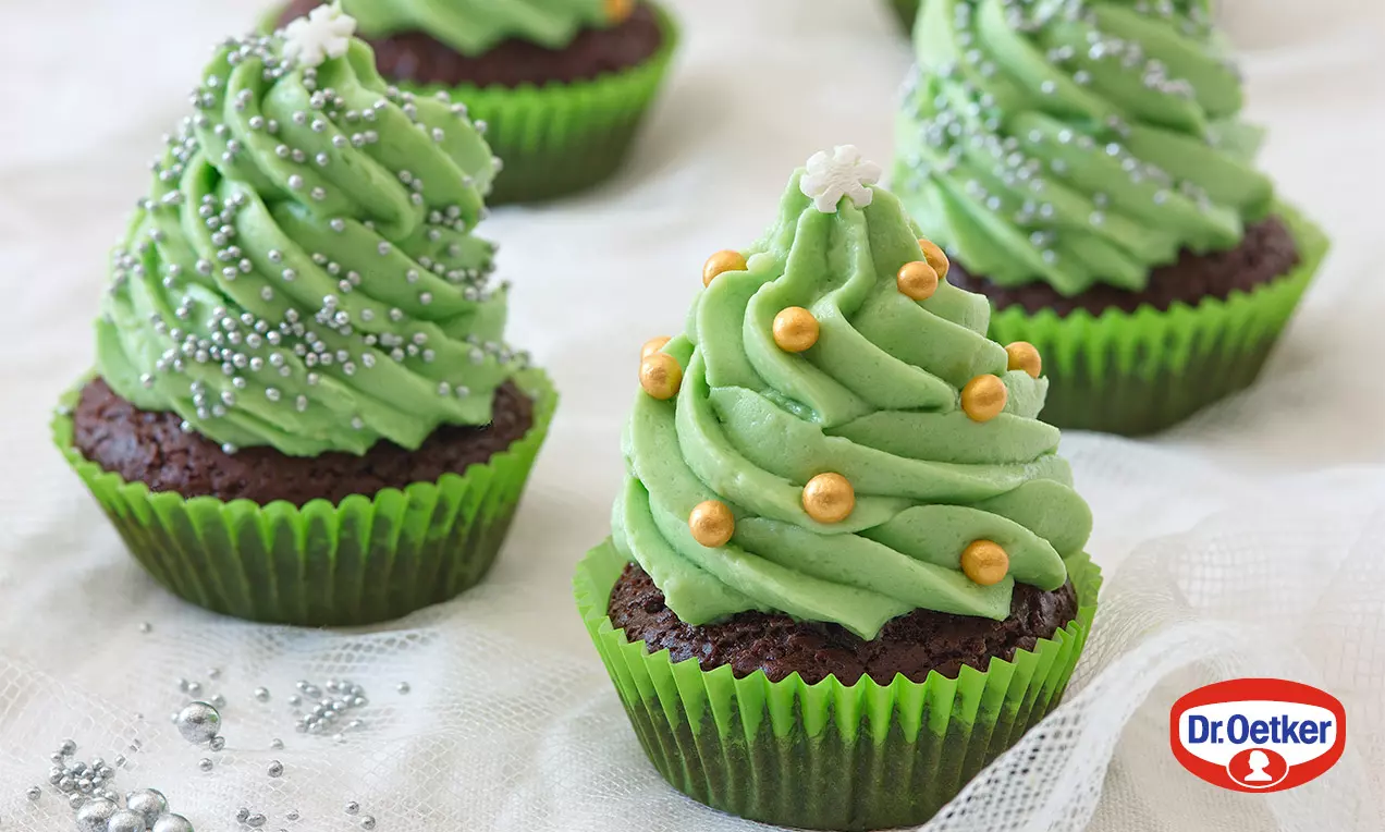 Čokoládové cupcakes v zelených košíčkoch, ozdobené zeleným krémom v tvare stromčeka, posypané perleťovými guľôčkami a hviezdičkami