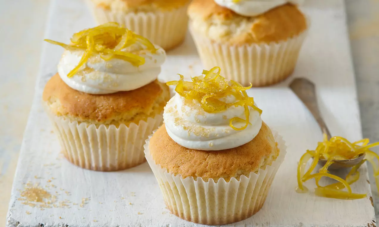 Cupcakes so zlatohnedým povrchom a krémovou bielou šľahačkou ozdobené tenkými prúžkami citrónovej kôry na drevenom podnose