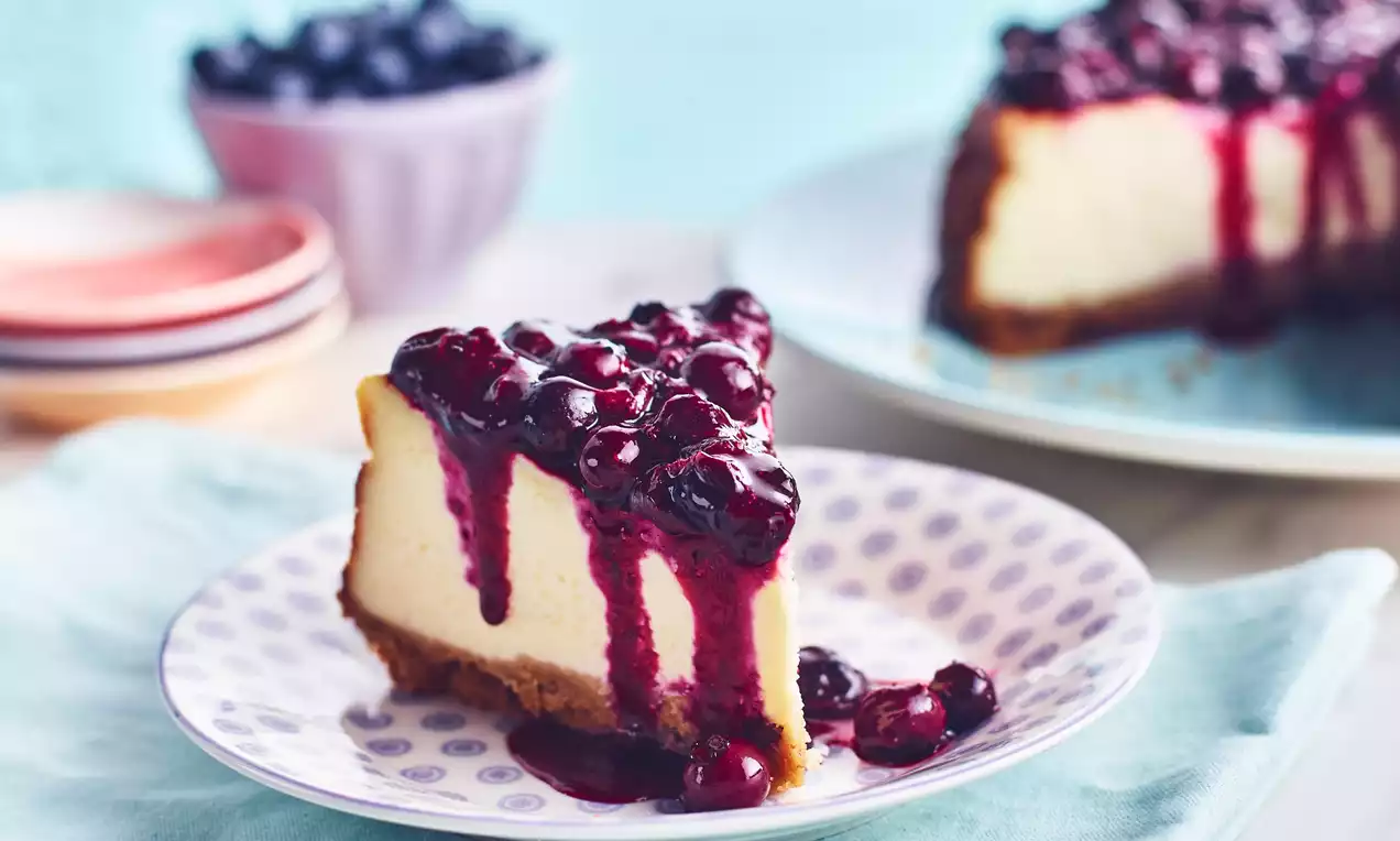 Krémový cheesecake s hladkou vanilkovou náplňou na sušienkovom základe, ozdobený lesklou borovicovou polevou na bodkovanom tanieri
