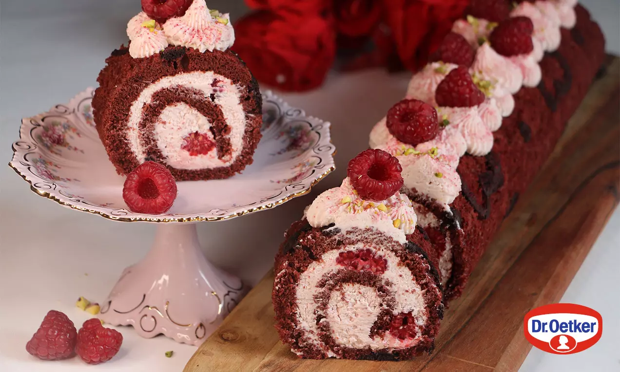 Malinová red velvet roláda s tmavočerveným piškótovým cestom, svetloružovým krémom, ozdobená malinami a šľahačkou na drevenej doske