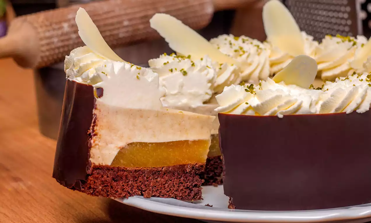Mango torta s vrstvou jasne žltého mangového pyré, nadýchaným krémom a čokoládovým okrajom, ozdobená šľahačkou a bielymi čokoládovými lupienkami