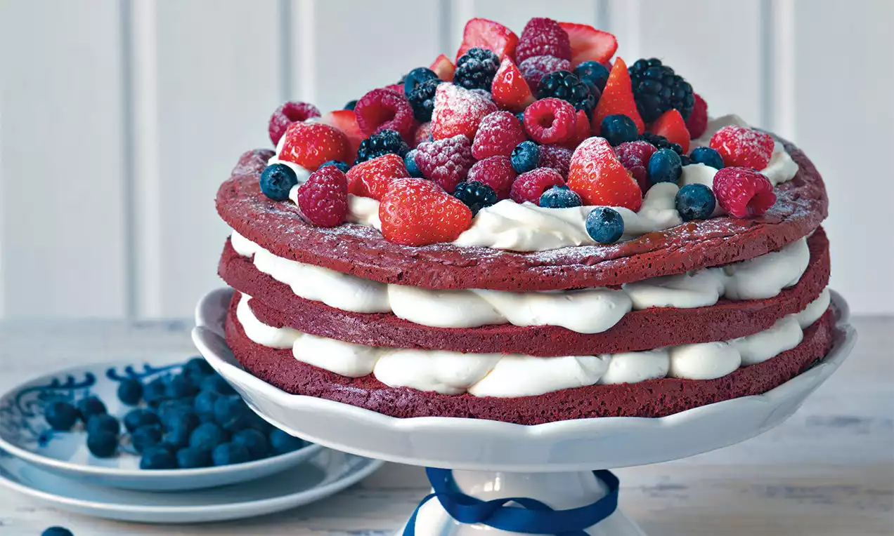 Trojvrstvový Red Velvet korpus tmavočervenej farby striedajúci sa so smotanovou plnkou, ozdobený čerstvým ovocím a jemne poprášený cukrom