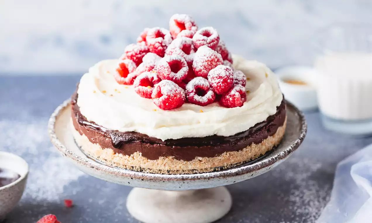 BB torta bez pečenia s vrstveným základom zo sušienok, nadýchaným krémom, čokoládovou polevou a čerstvými malinami posypanými práškovým cukrom