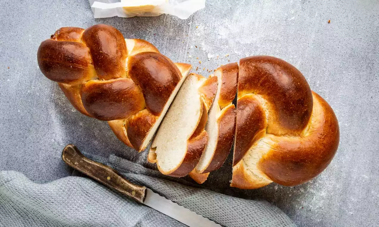 Zlatohnedý vegan pletenec s lesklým povrchom, nakrojený na niekoľko krajcov, položený na sivom podklade vedľa noža a utierky
