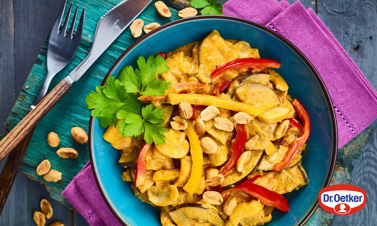 Vegánske zeleninové kari v tyrkysovej miske, s kúskami farebnej zeleniny v krémovej kari omáčke, ozdobené arašidmi a petržlenovou vňaťou