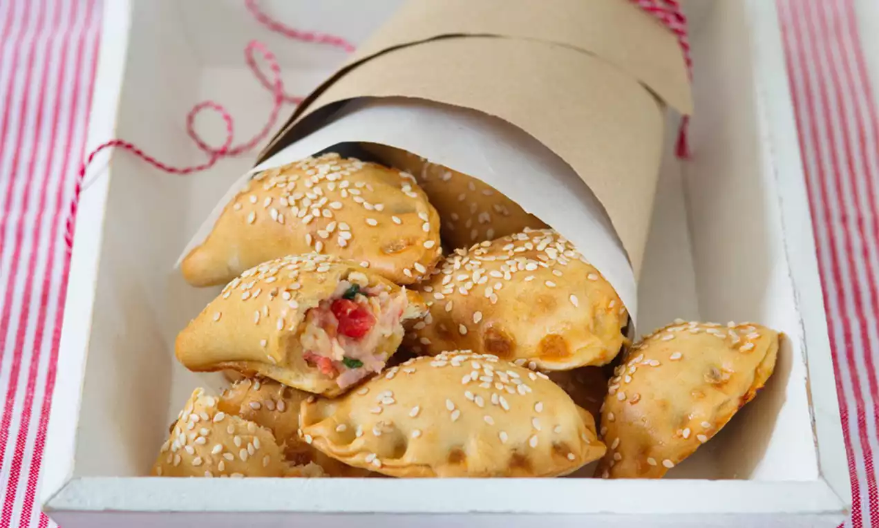 Zlatohnedé mini calzone s chrumkavým povrchom, posypané sezamovými semienkami, usporiadané v papierovom kornútku na bielej drevenej tácke